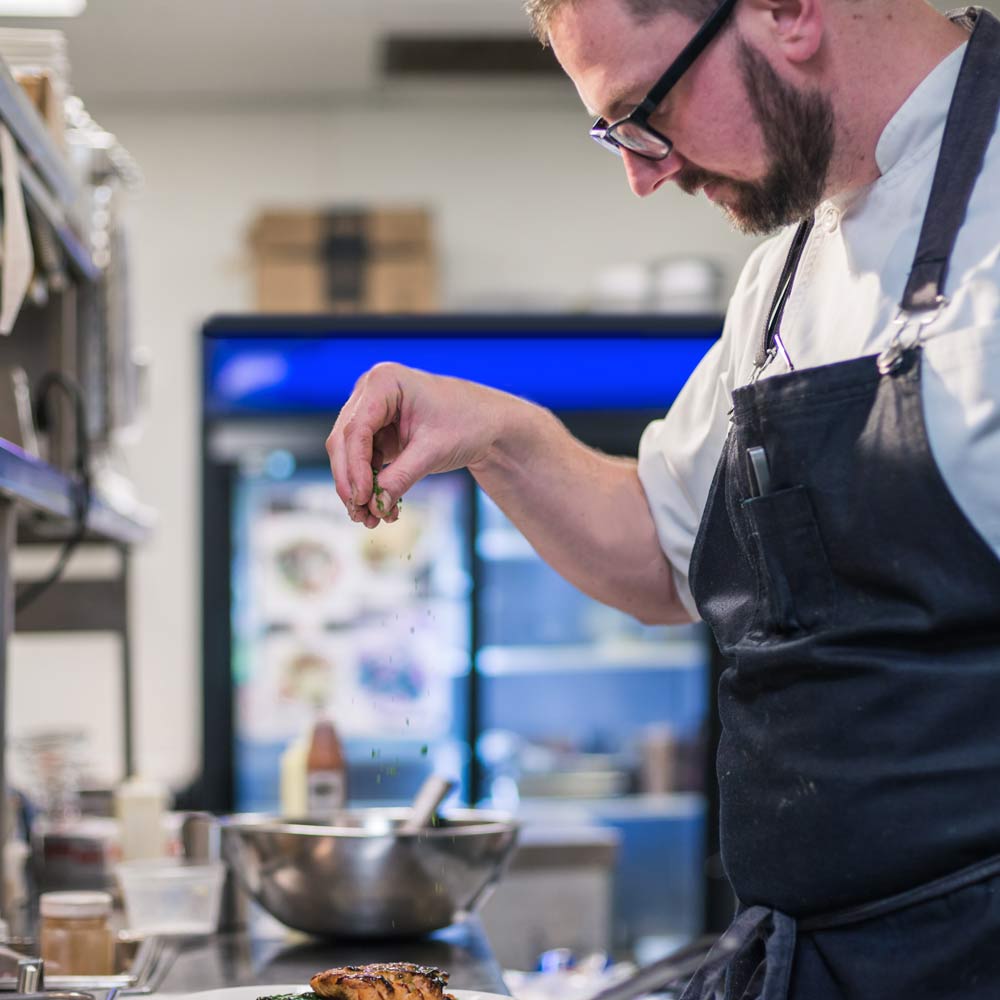 Old Kinderhook's chef sprinkling seasoning on a dish